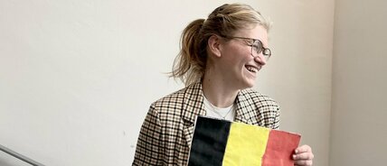 Zu sehen ist eine Lehrerin. Sie ist blond. Sie lacht. Sie hält eine belgische Flagge in der Hand.